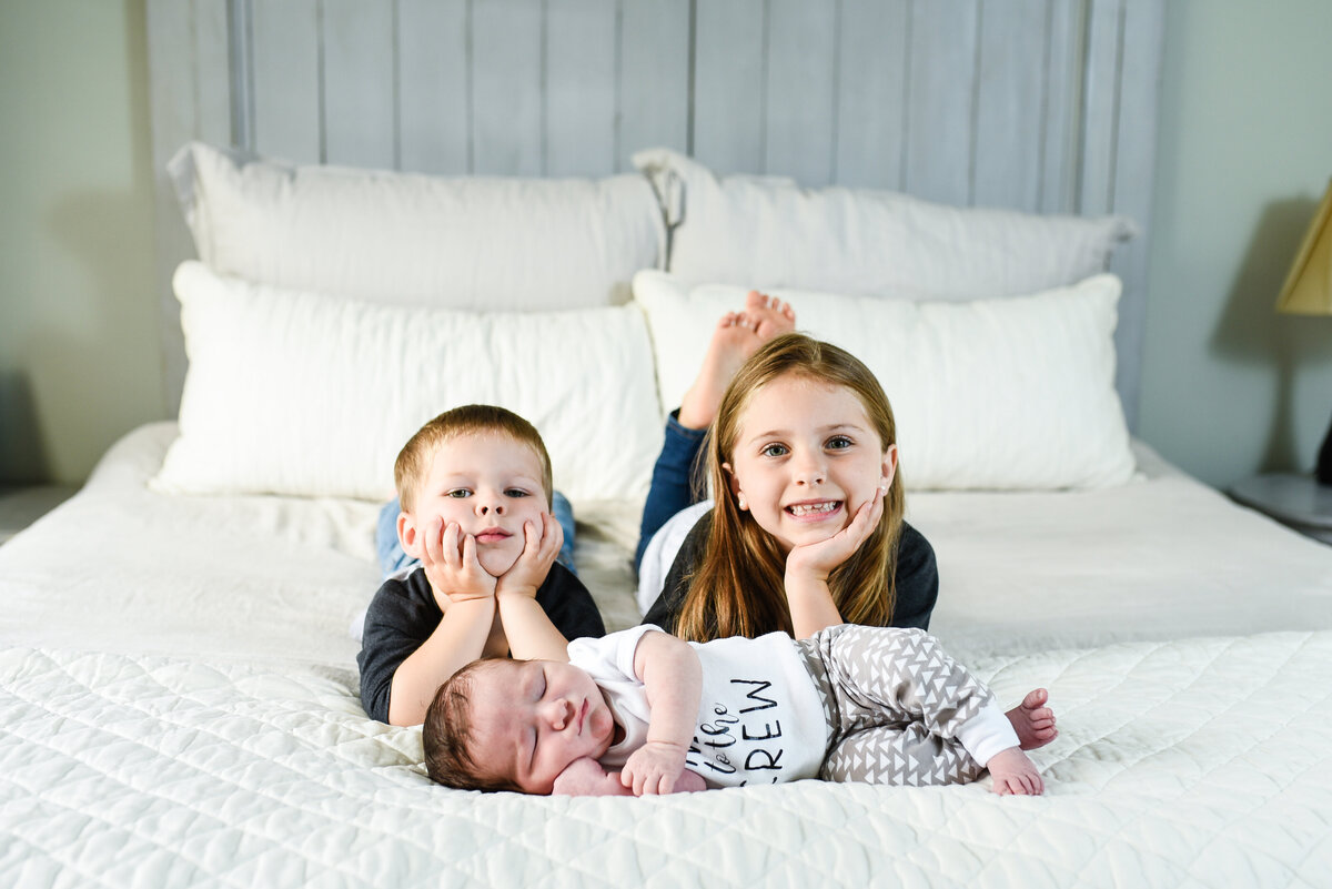 Beautiful lifestyle newborn photography: newborn boy and his siblings on their parents bed at home in Mississippi