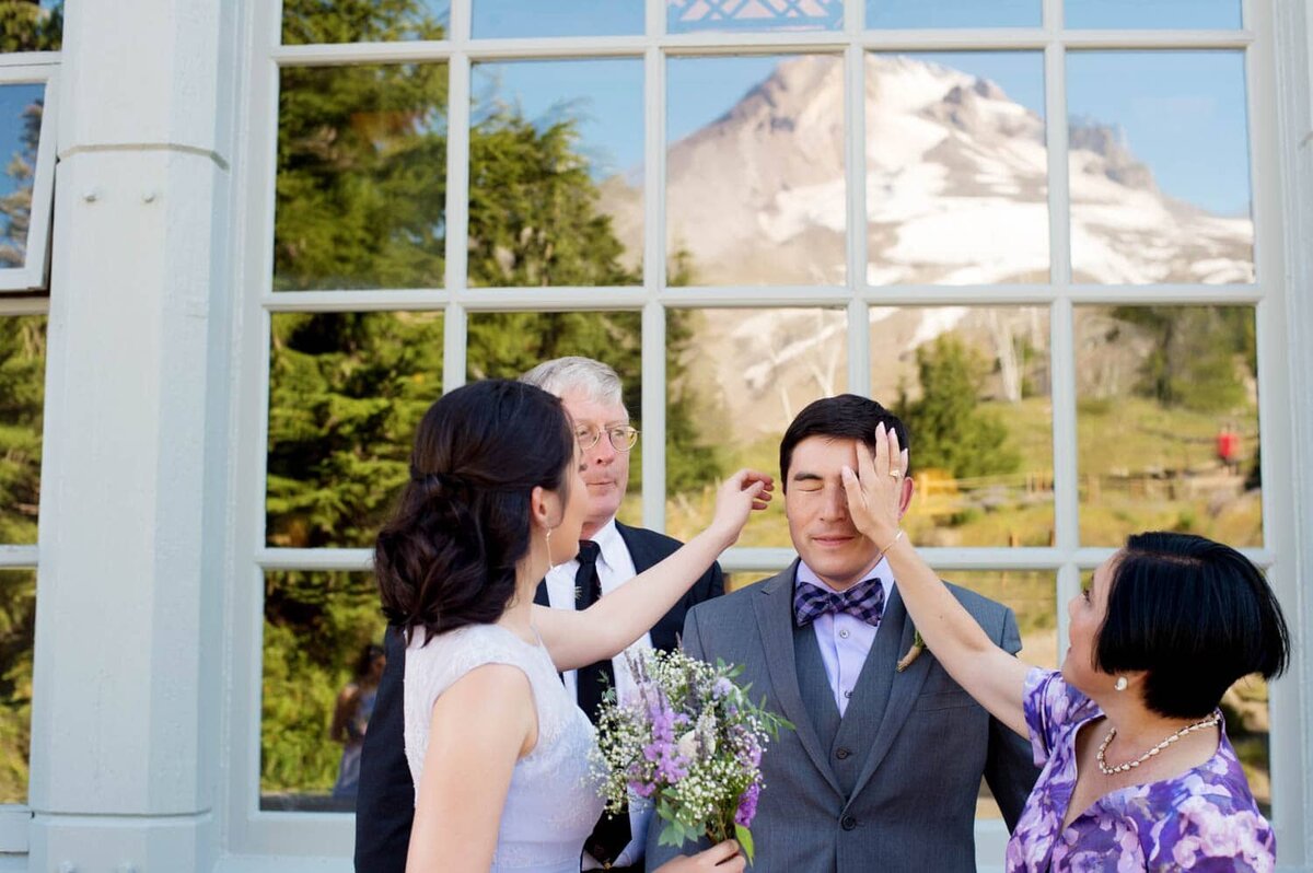 a mom and sister fix a groom's hair before his wedding with mt hood in background