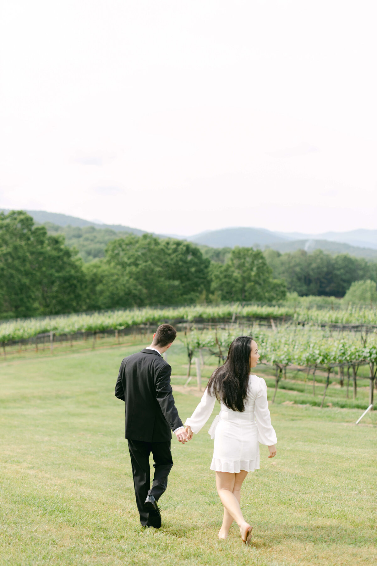 A bride and groom walk casually through a vineyard.