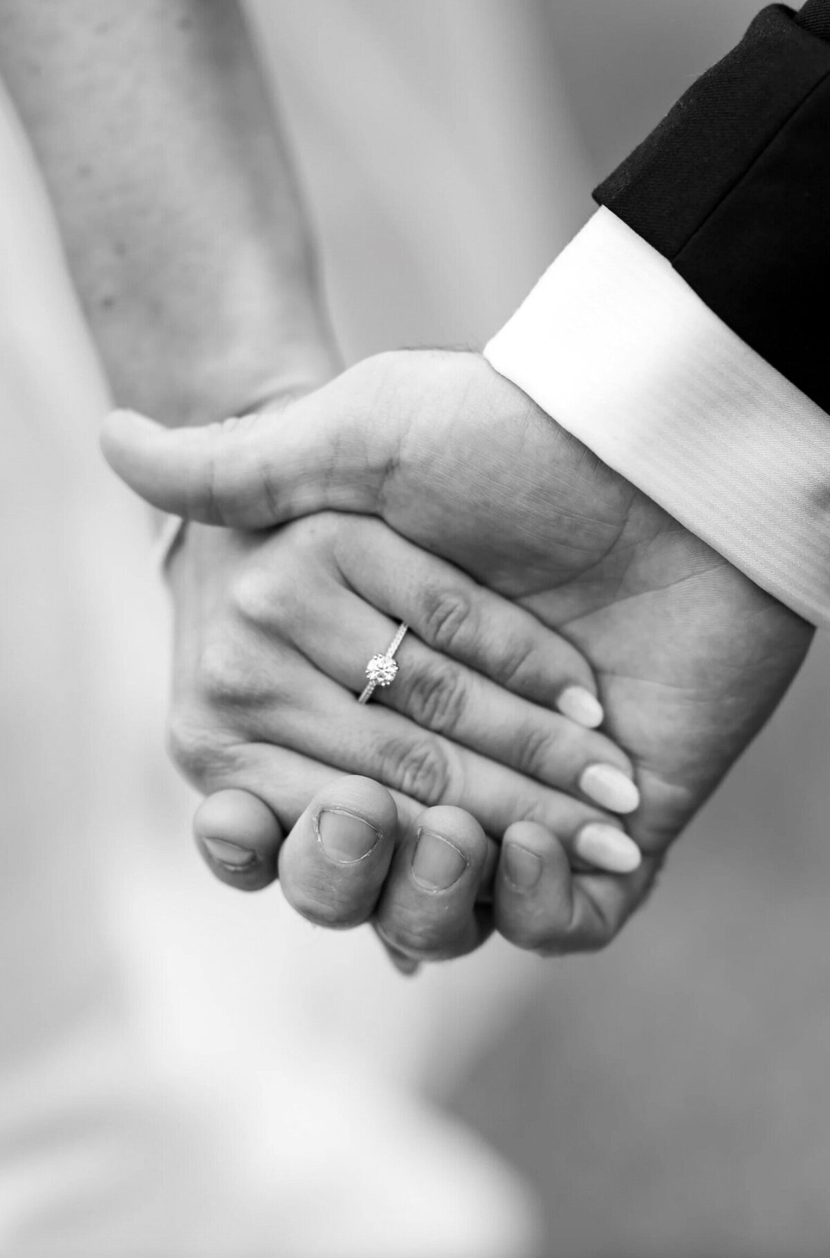 Photo of a bride and groom, holding hands displaying her engagement ring on the grounds of Brigalias in New Jersey