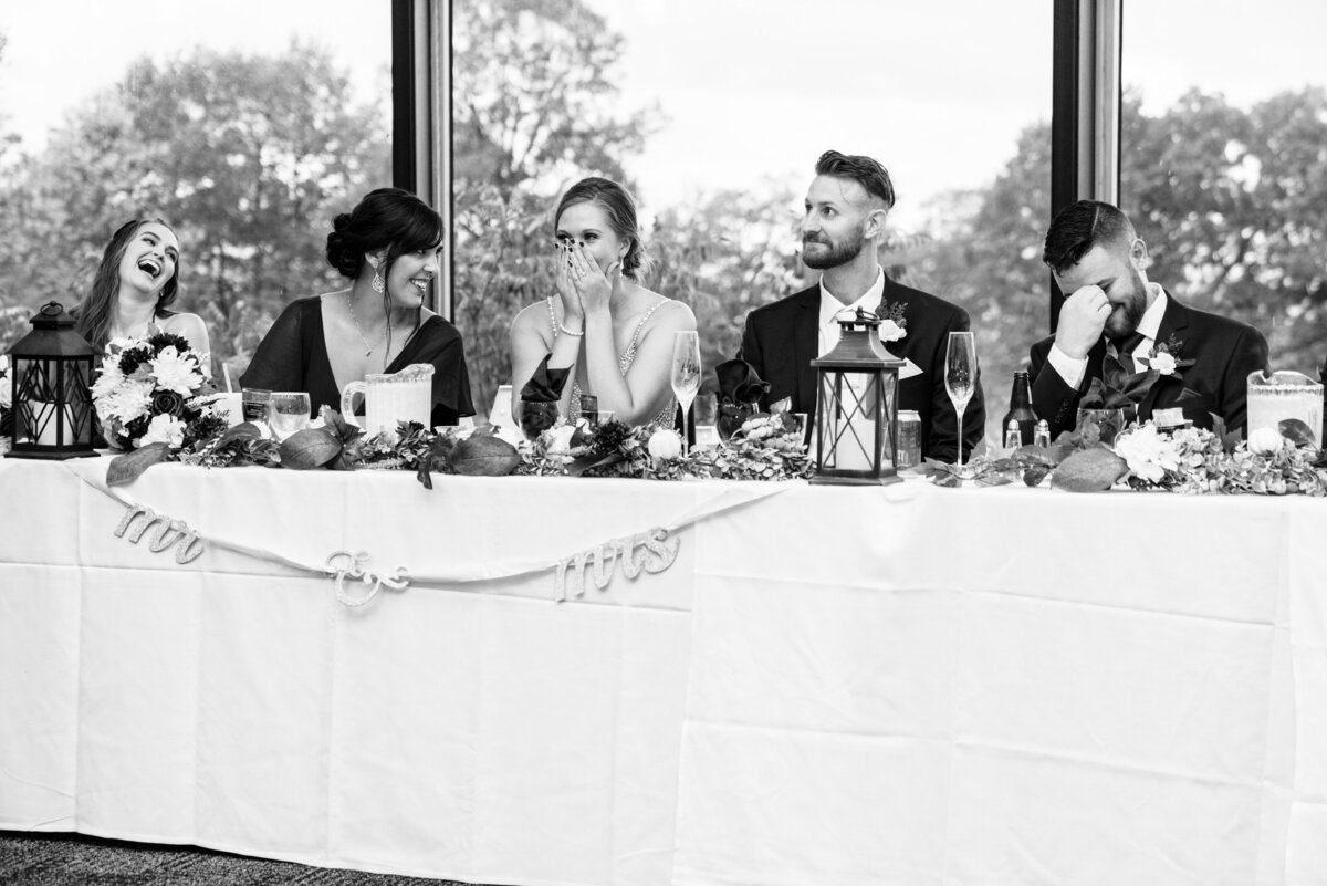 Bride and groom and party laugh at head table.