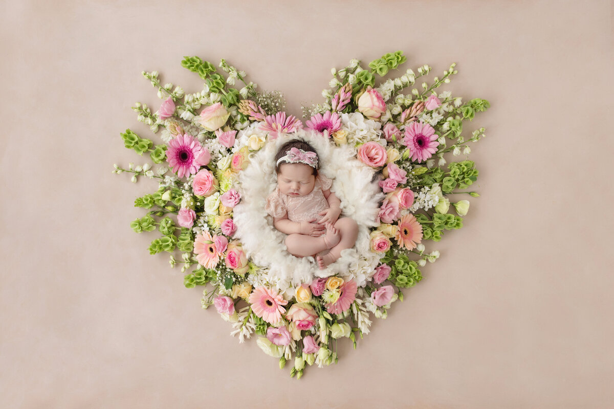 A NJ Newborn Photography image of a newborn baby sleeping in the center of a heart shaped floral design