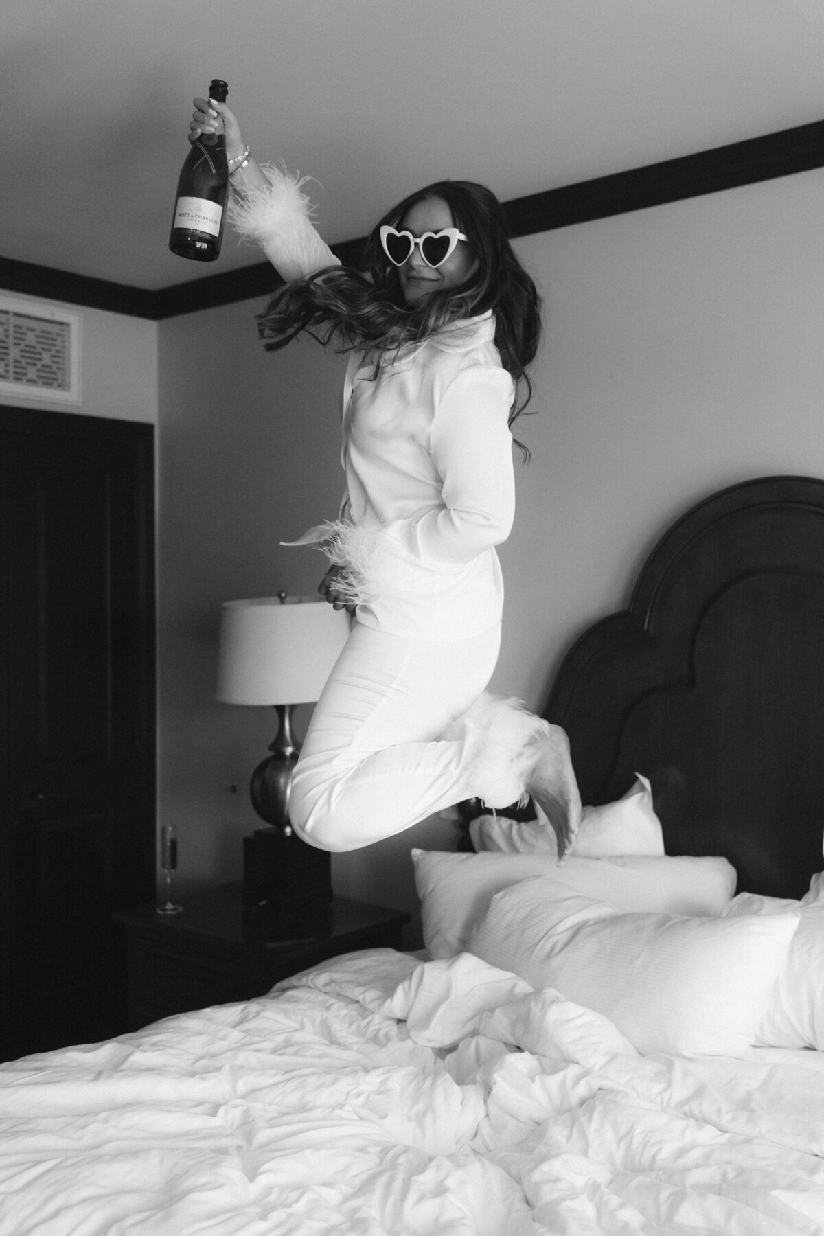 Bride with white heart sunglasses jumping with champagne