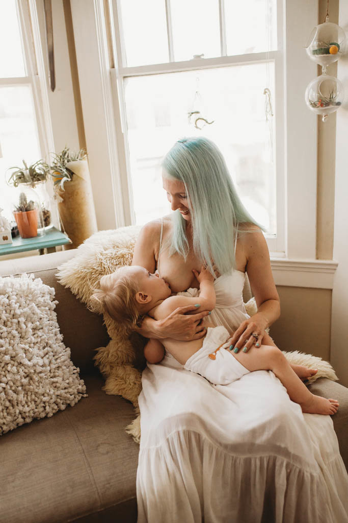 Bay area mom with teal hair breastfeeds baby at intimate motherhood session in home