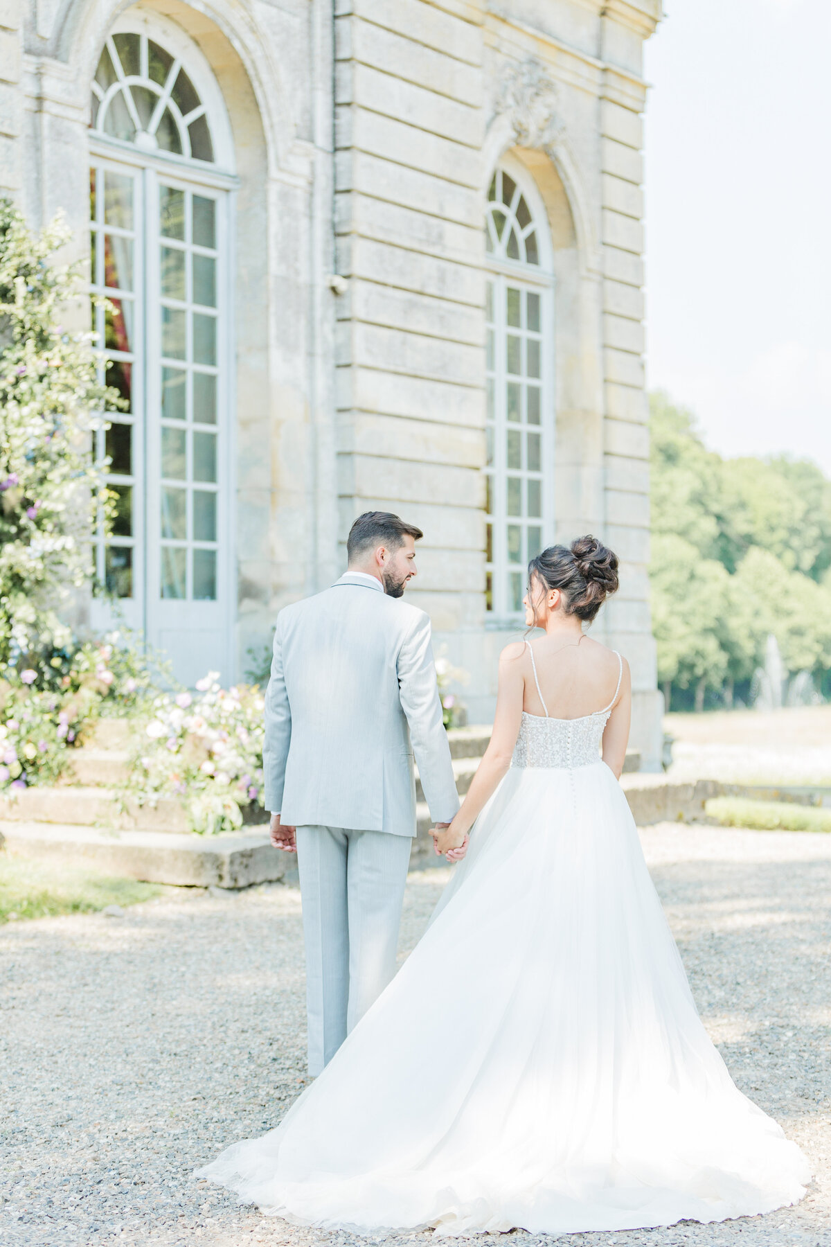 Lia Rose Weddings, based in Rhode Island captures an intimate moment between a bride and groom at their Paris, France destination wedding. The image is of the bride and groom's back. They are holding hands and looking at each other. Captured by destination wedding photographer Lia Rose Weddings