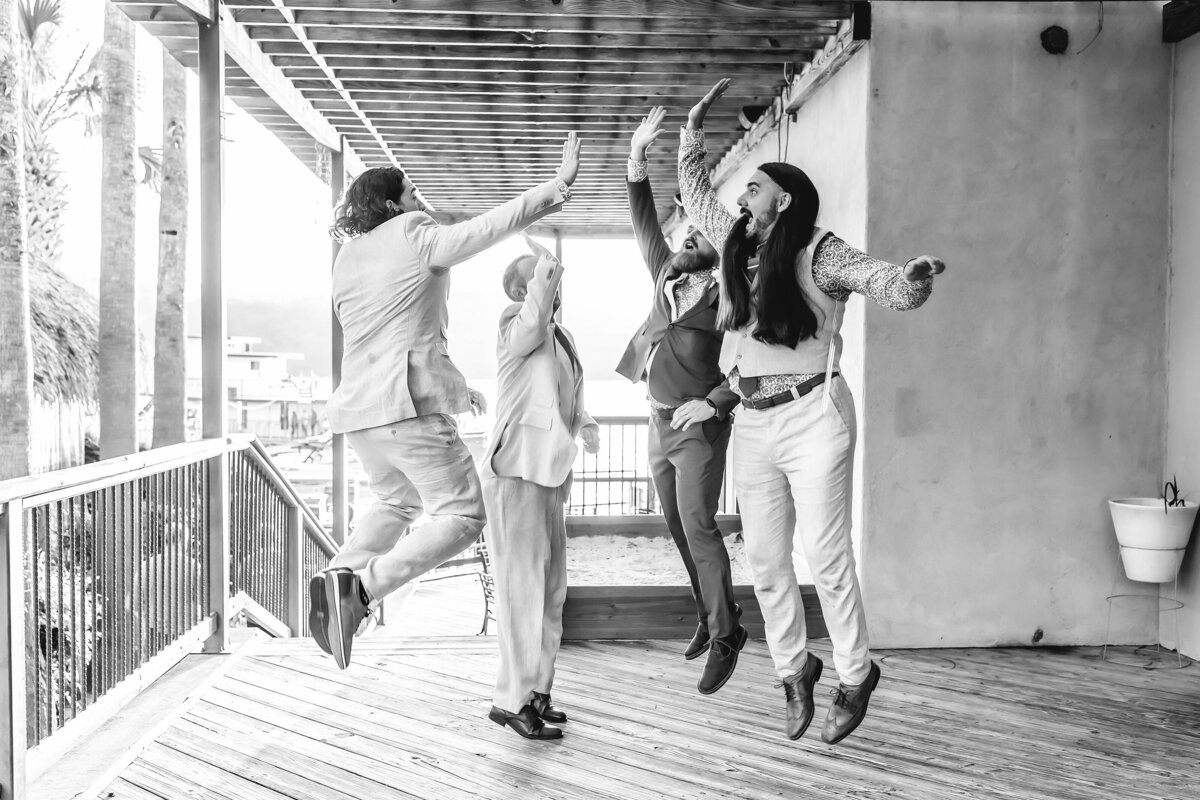 Groom and groomsmen jumping while high fiving on the patio at Abel's on the Lake in Austin , Texas