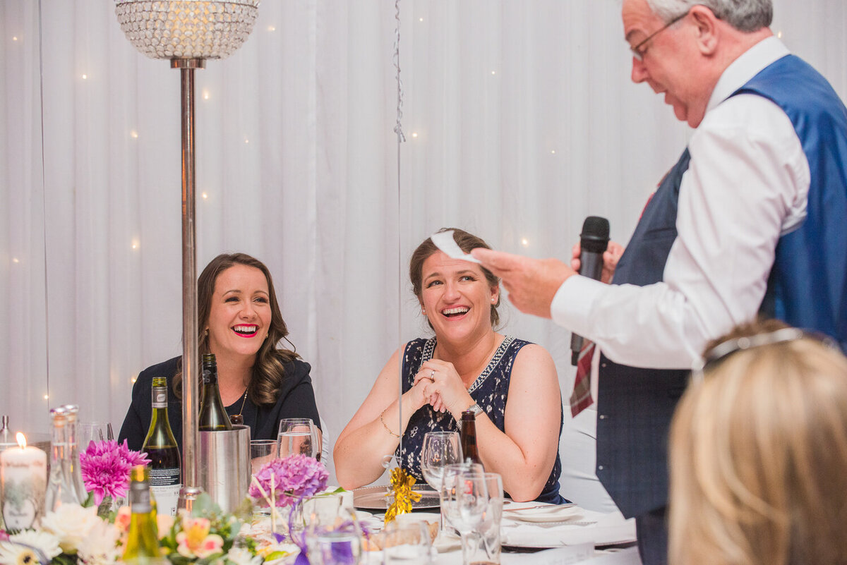 Dad giving wedding speech while the two brides laugh
