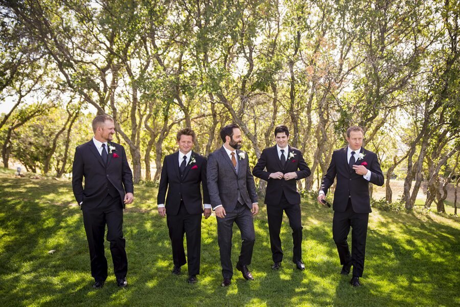 A groom and four groomsmen walk toward the camera, candidly fixing their suits.