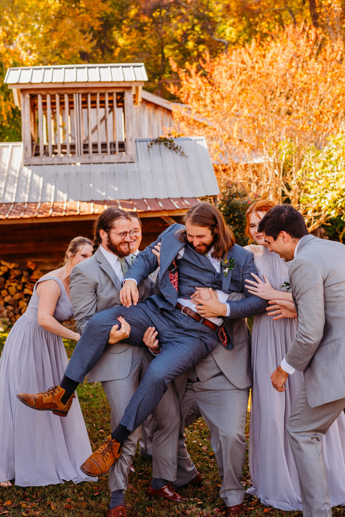 Photo of a Groom being picked up in a playful manner from his wedding party