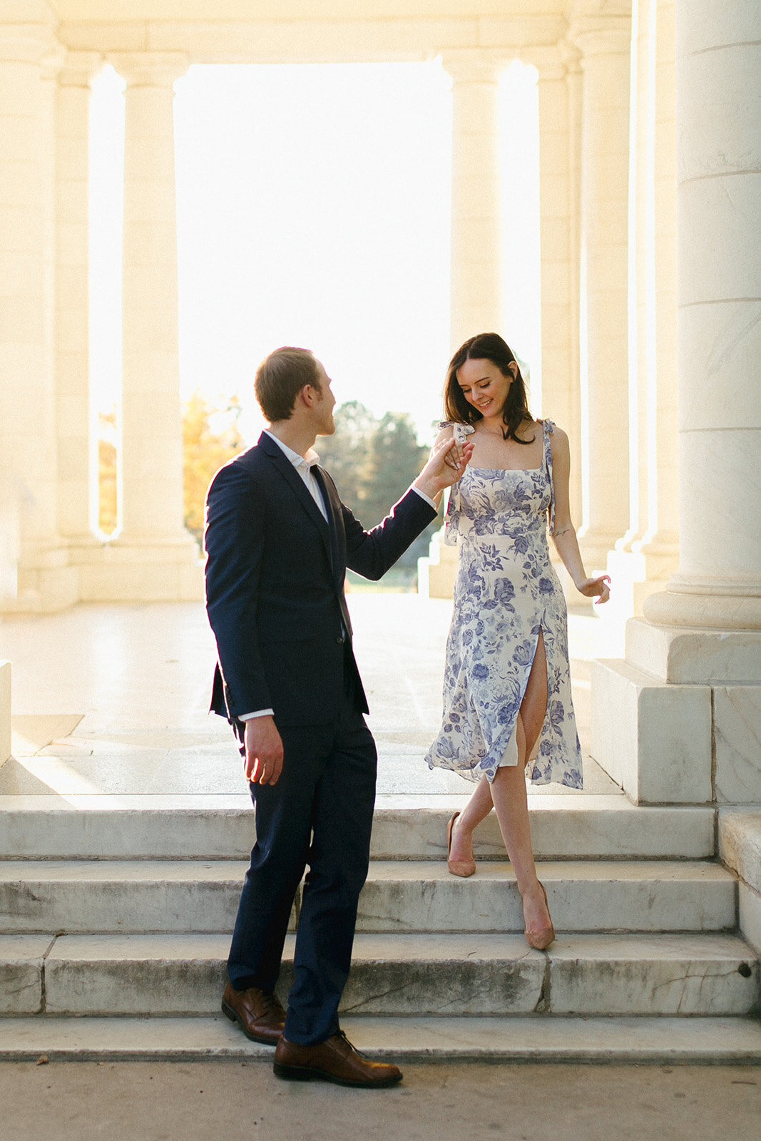 Man leads woman down steps at Cheesman Park Pavilion during engagement session.