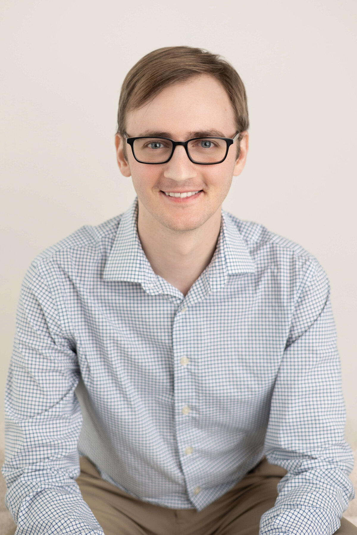 Man in glasses and collared shirt smiling on light background