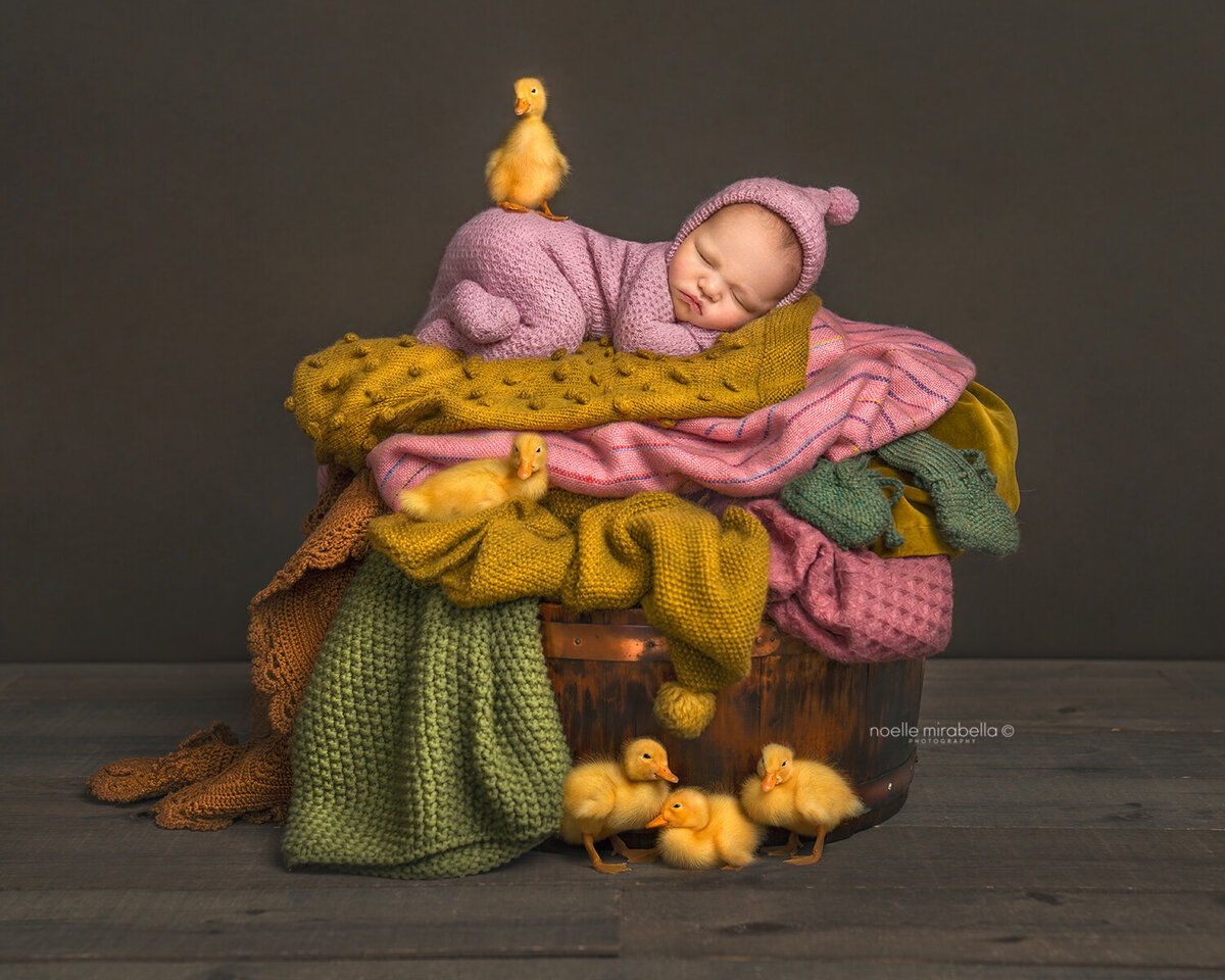 Baby sleeping in colourful pile of laundry with baby ducklings.