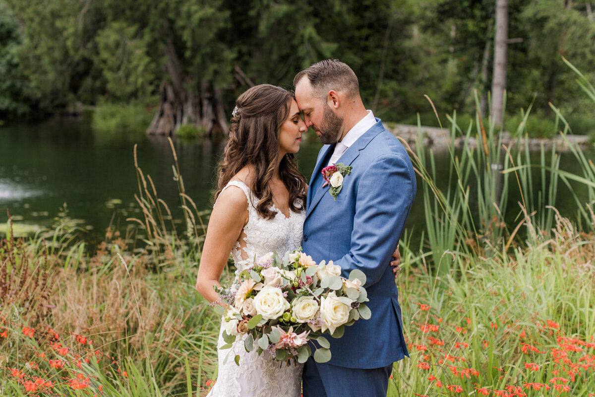 Bride-and-groom-kiss-in-front-of-lake-at-forest-outdoor-venue-Gray-Bridge-Sultan-in-Snohomish-WA-photo-by-Joanna-Monger-Photography