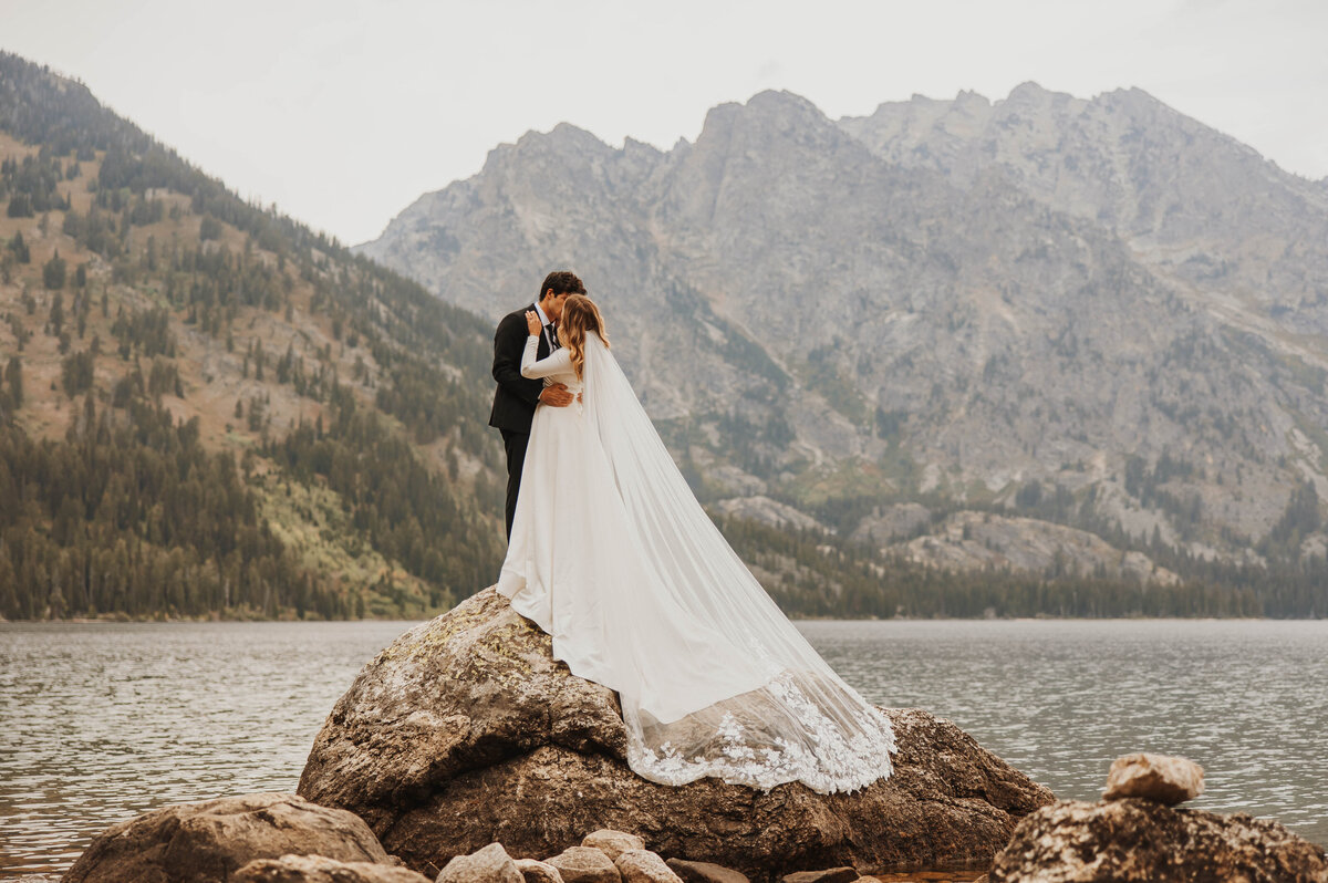 bride and groom kissing on large rock in lake