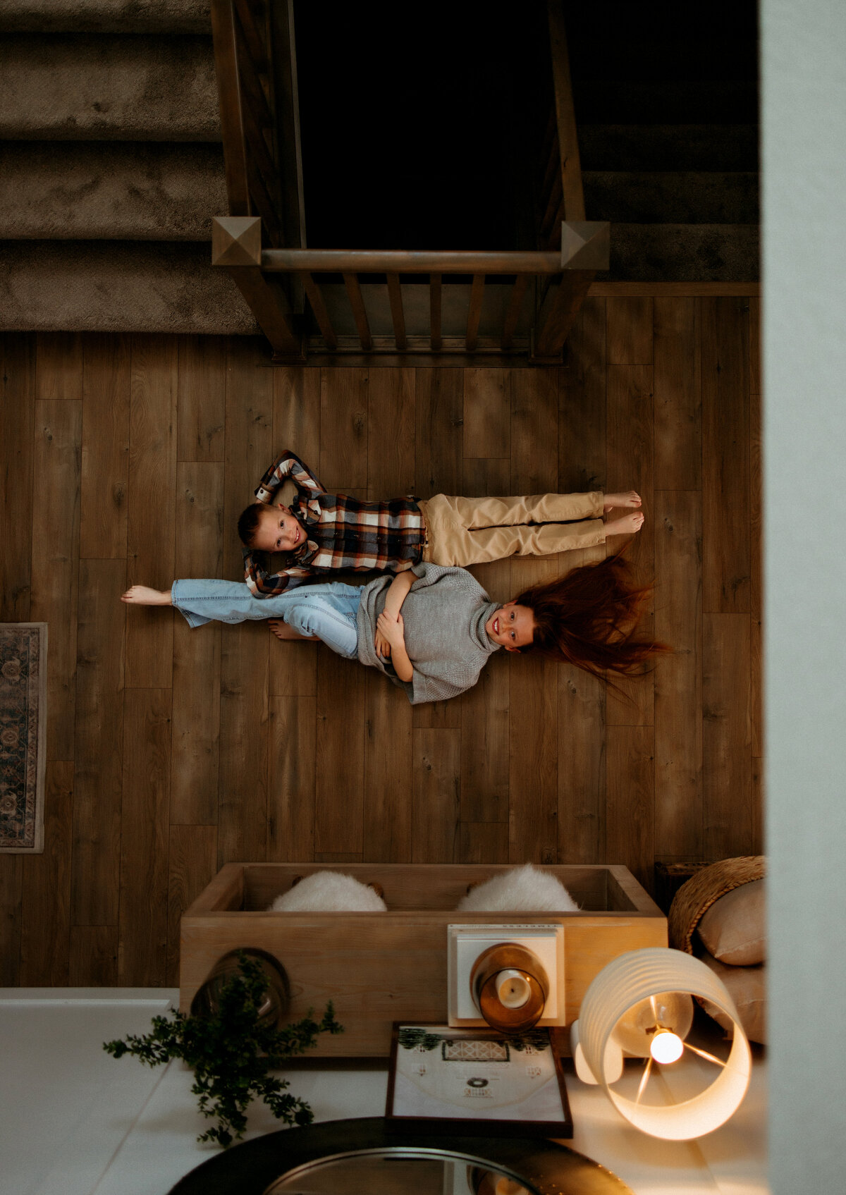 birds eye view of two kids laying on  wooden floors while looking up at camera for in home photos
