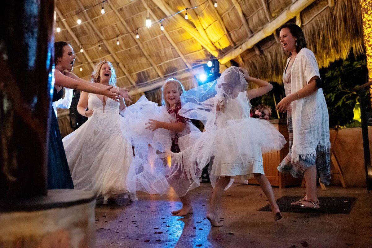 two little girls rip the tulle from the bride's wedding dress and run around dancing with it