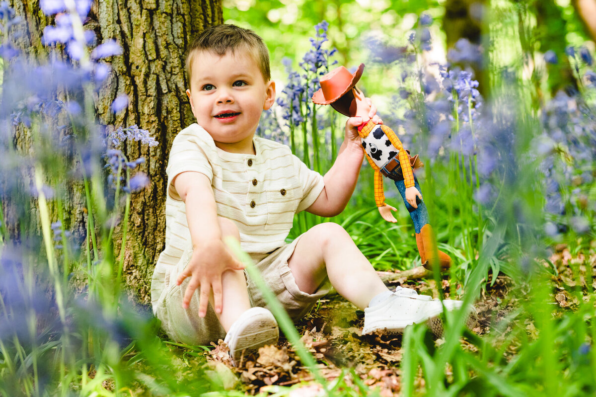 Little boy sat in the bluebells with woody from toy story