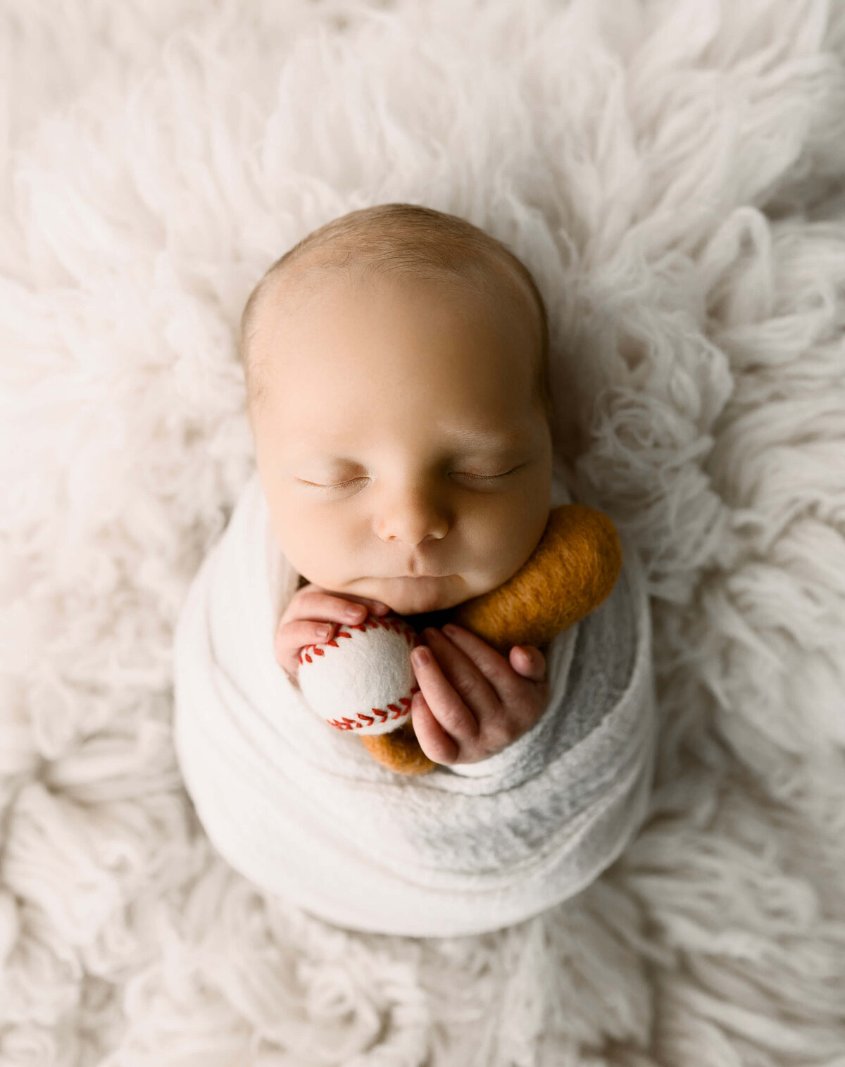 Newborn baby boy wrapped and holding a baseball and bat
