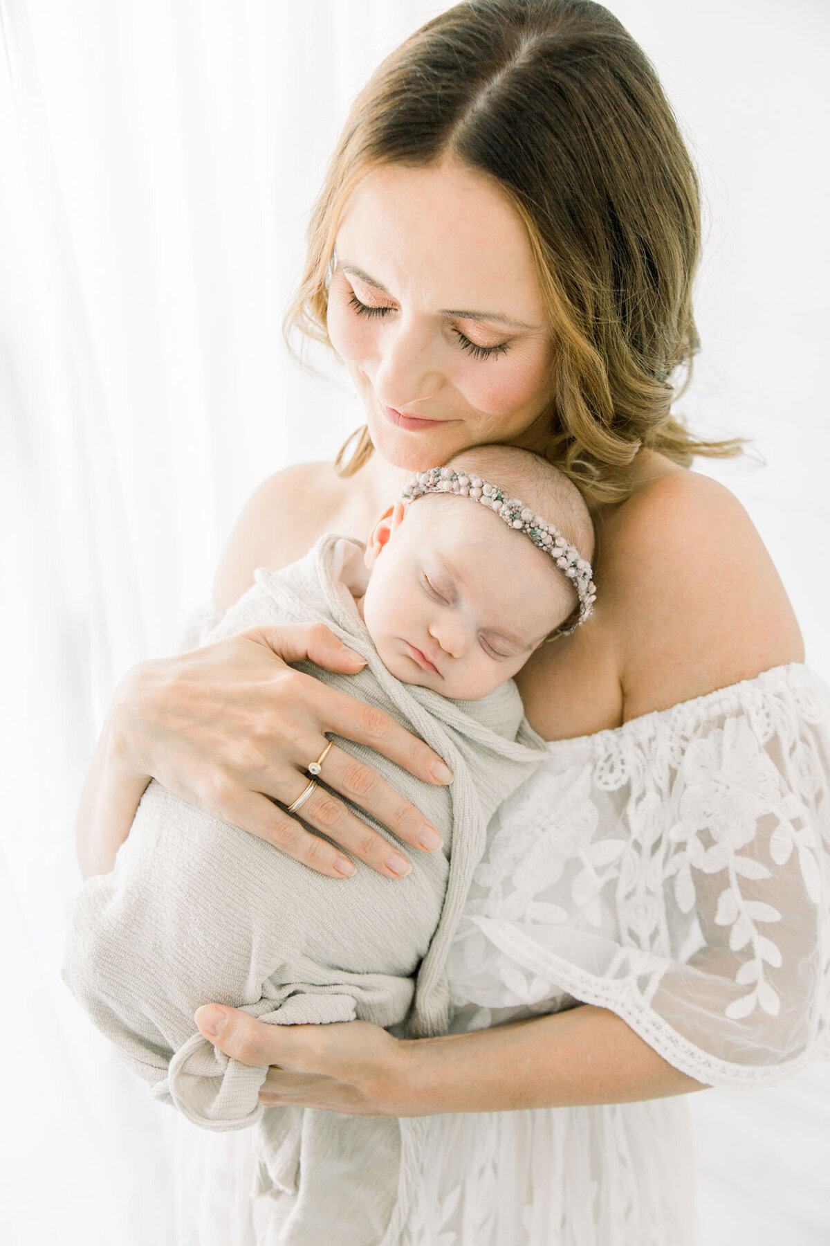 Babyfotoshooting in Gütersloh Nähe Verl: Mama im weißen Spitzenkleid mit Neugeborenem auf dem Arm.