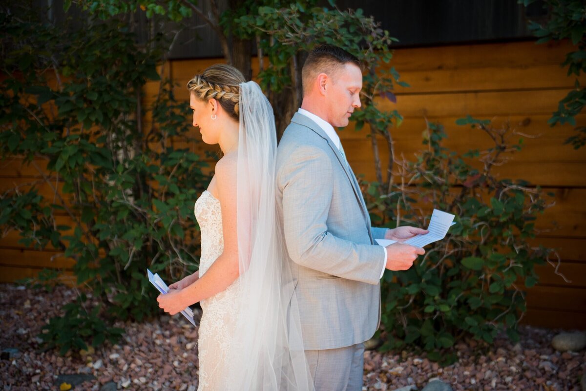 A bride and groom stand back to back without seeing each other as they read letters to one another.