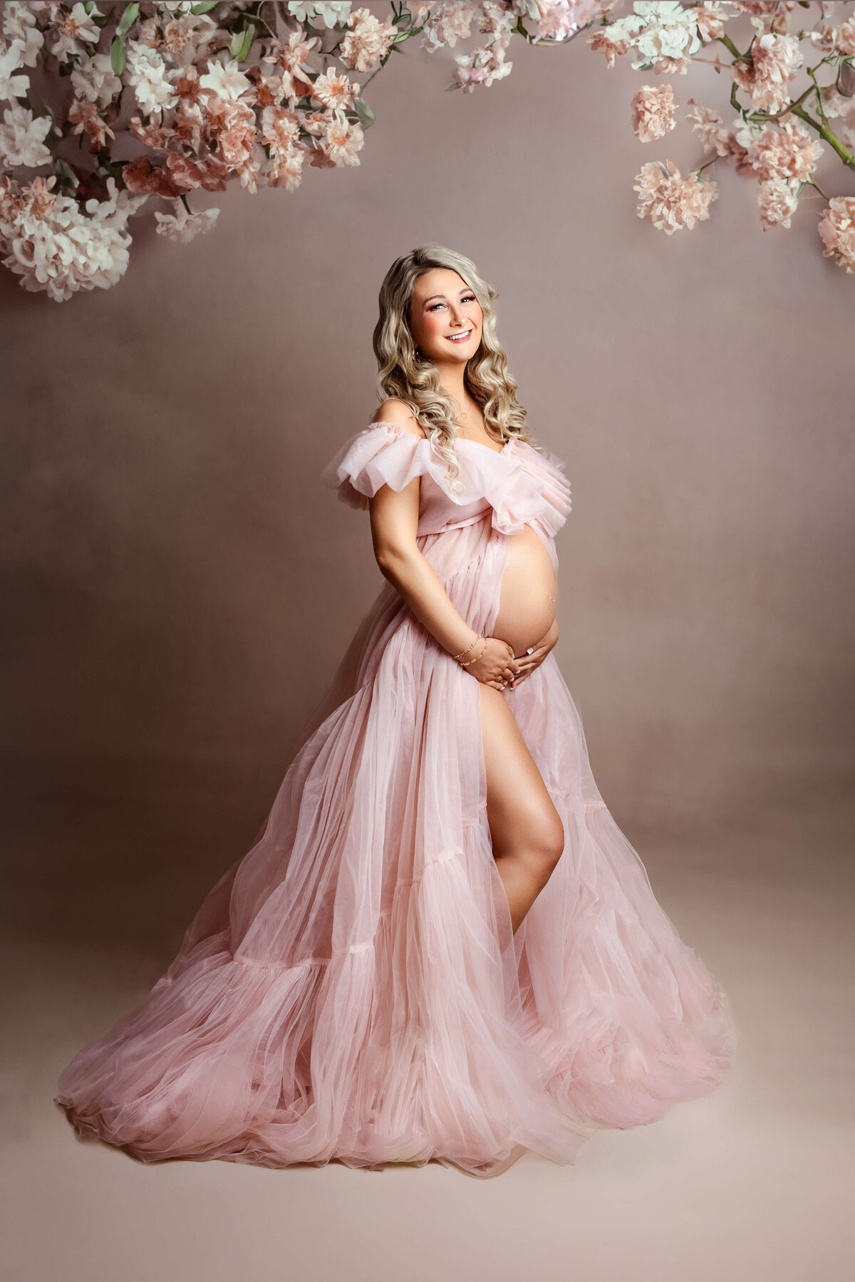 pregnant mother wearing a pink designer maternity gown with pink flowers on top at a maternity photo shoot in northern va