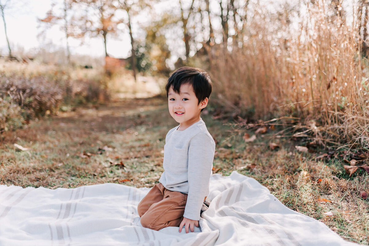 A toddler boy kneels on a white blanket in Northern Virginia
