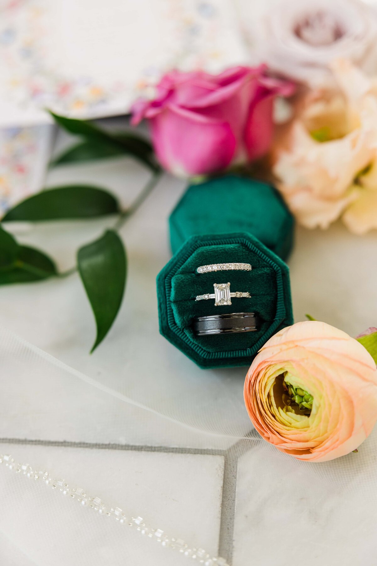 An elegant engagement ring inside a green velvet box surrounded by colorful flowers and a wedding invitation, meticulously arranged by a top wedding planner from Des Moines.