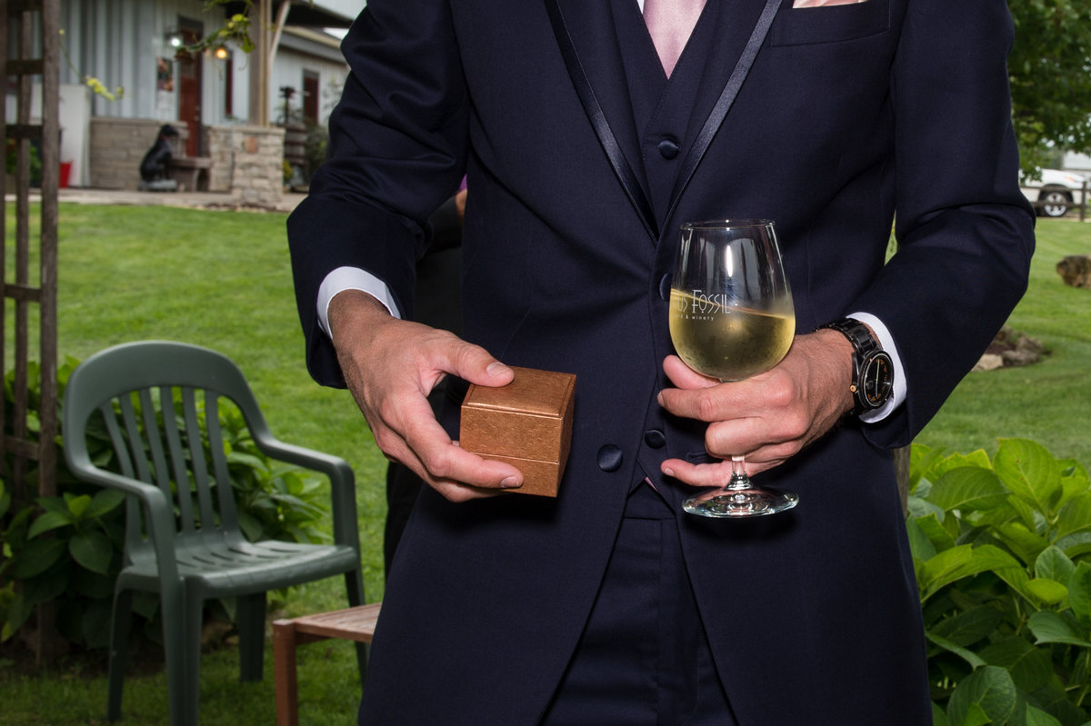 groom holding rings and wine at vineyard wedding