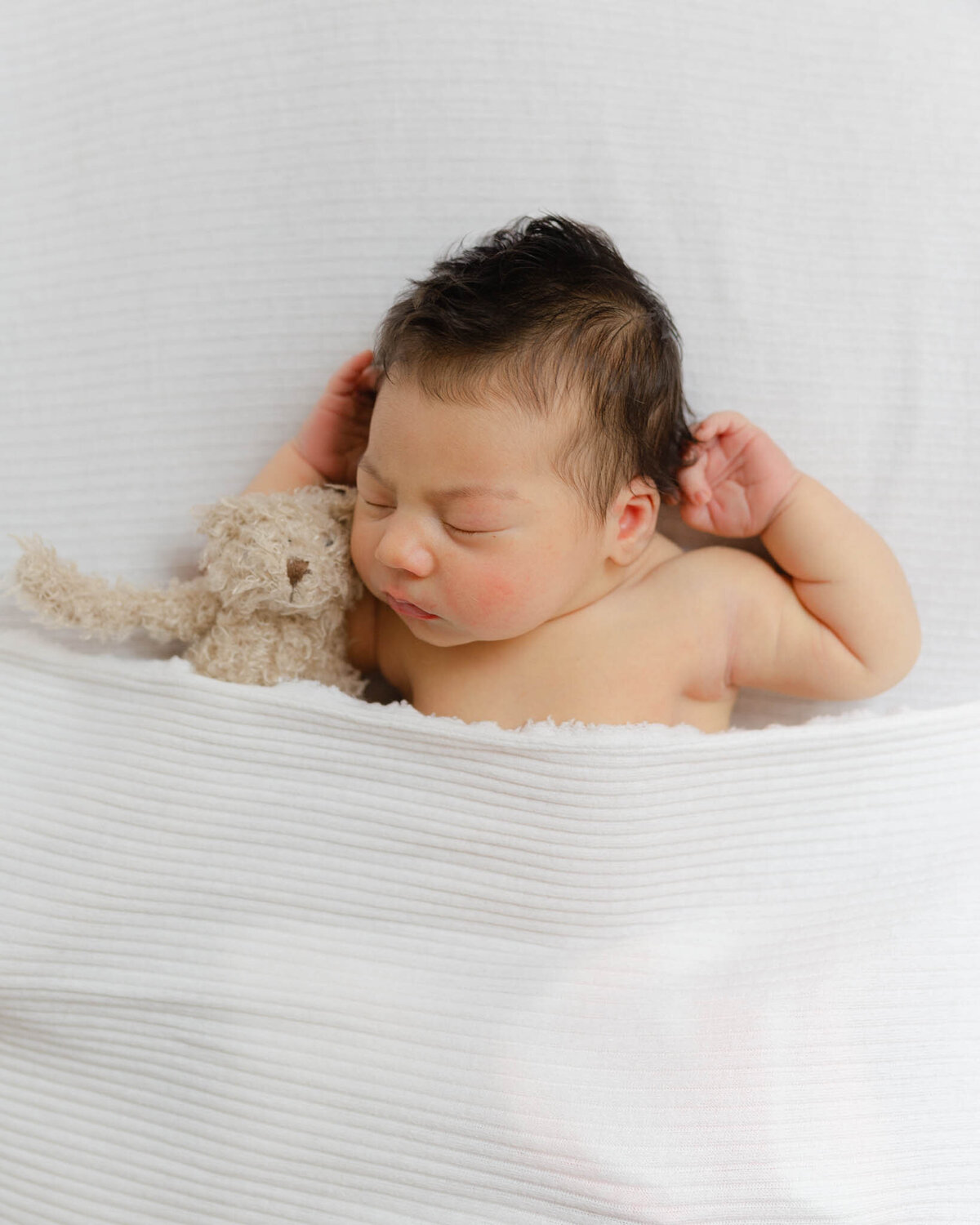 newborn baby sleeping on white with hands behind head