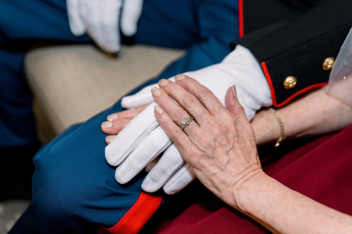 Bride's hand gently resting on groom's hand in Marine Corps dress blues and white gloves, captured during their 50th wedding anniversary celebration.