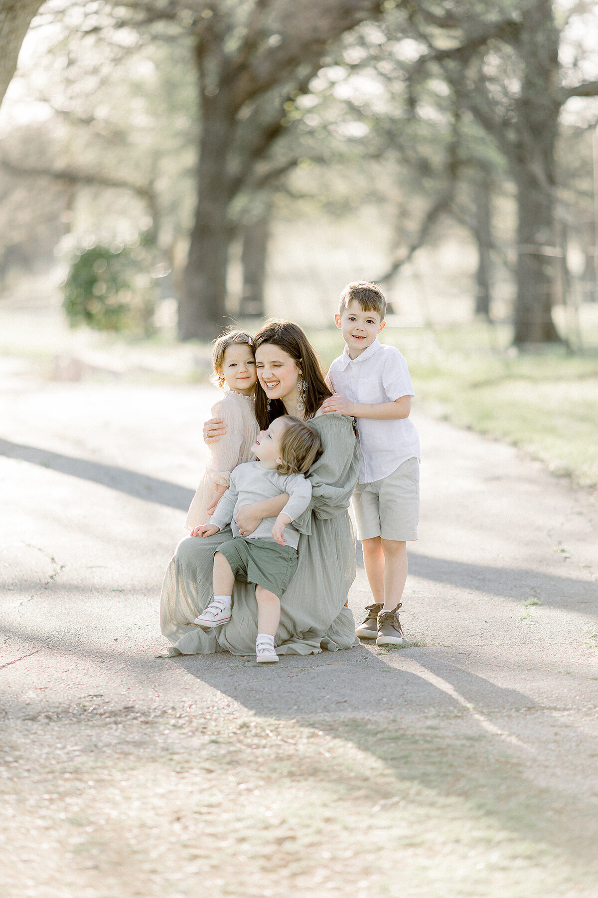 A mother with her 3 children snuggling with them at a Fort Worth park for her new family portraits.