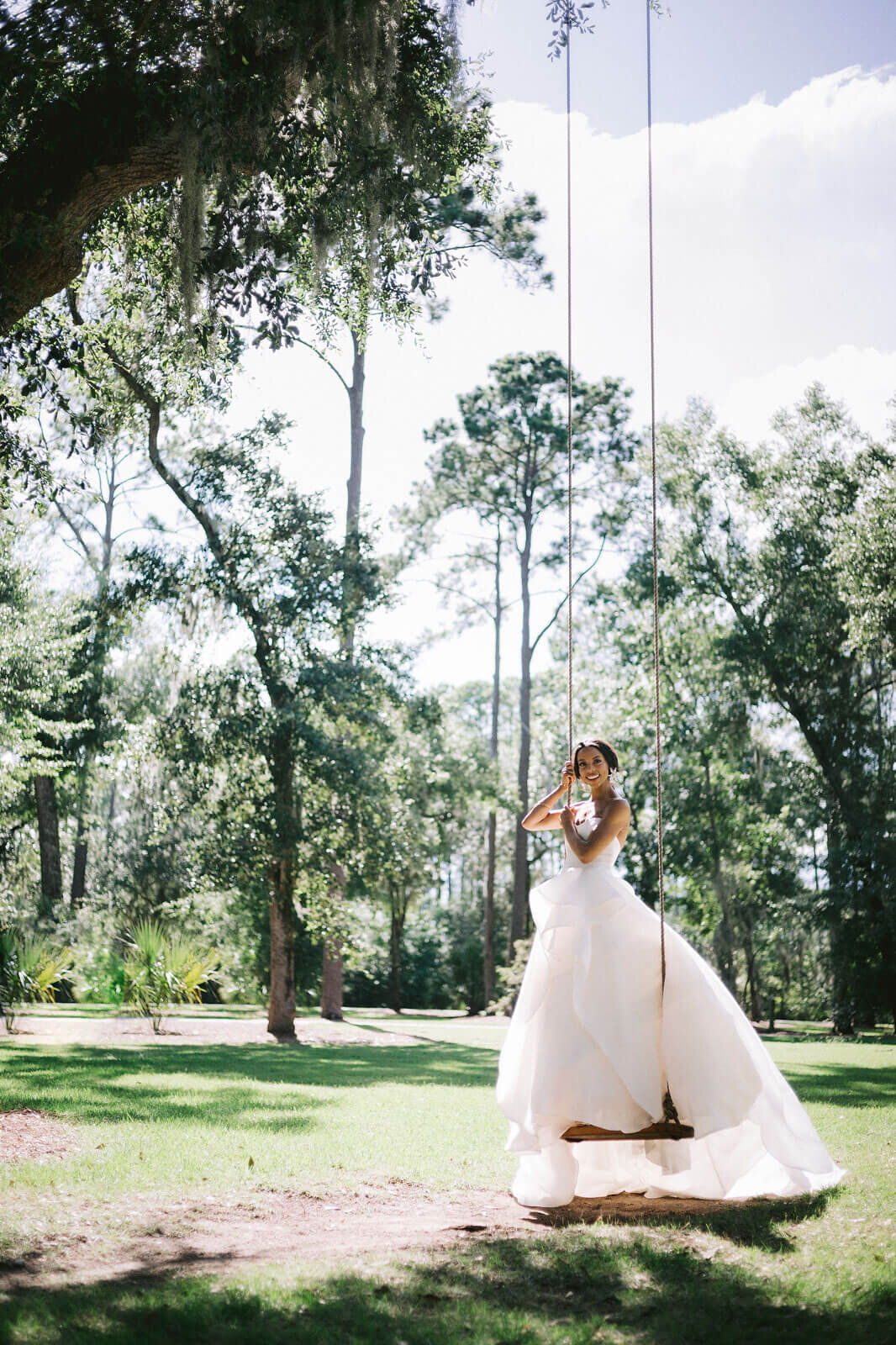 The bride is standing in a swing amongst the trees in Montage at Palmetto Bluff. Destination wedding image by Jenny Fu Studio