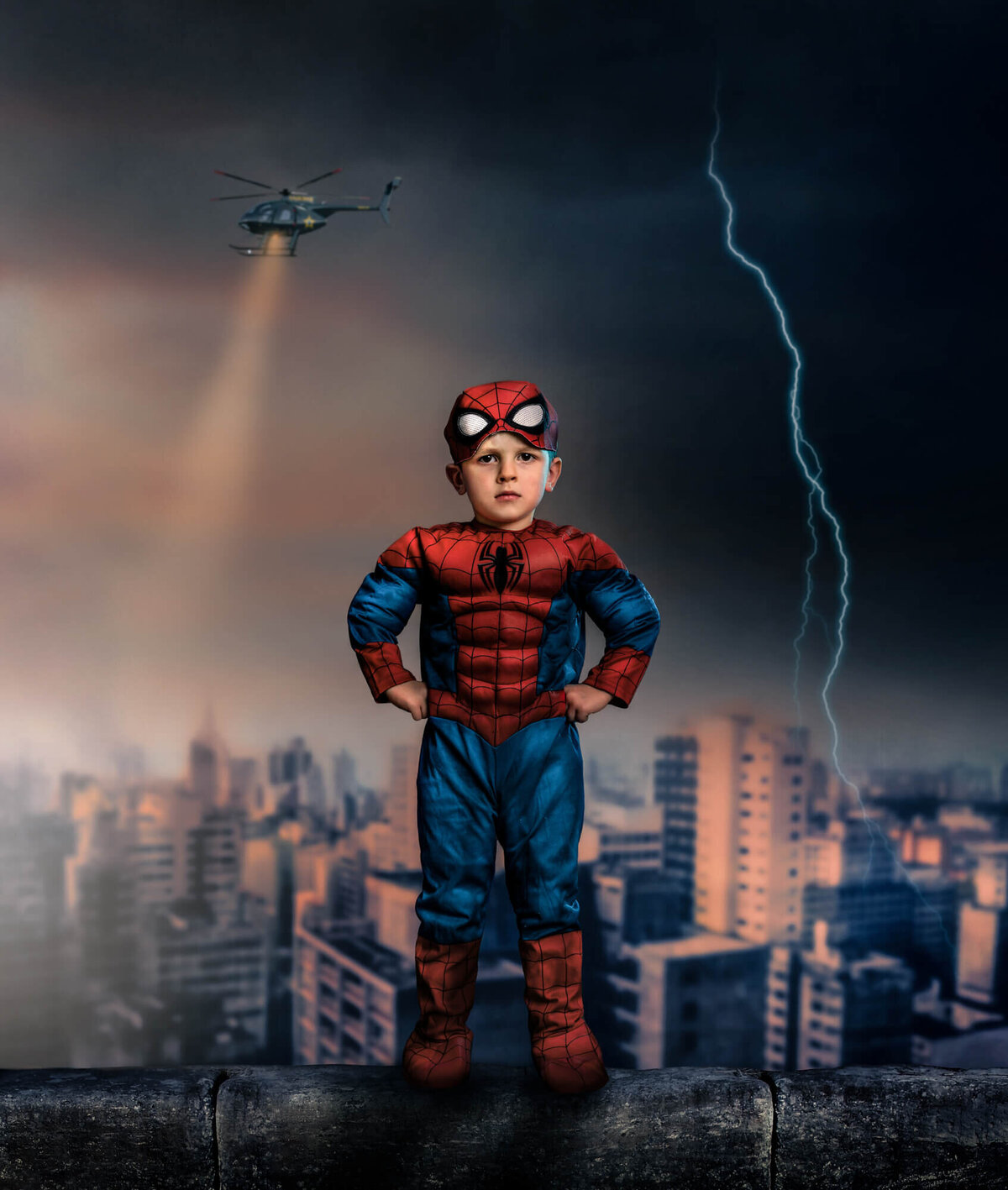 A young boy stands on a building ledge dressed as SpiderMan while lightening strikes behind him