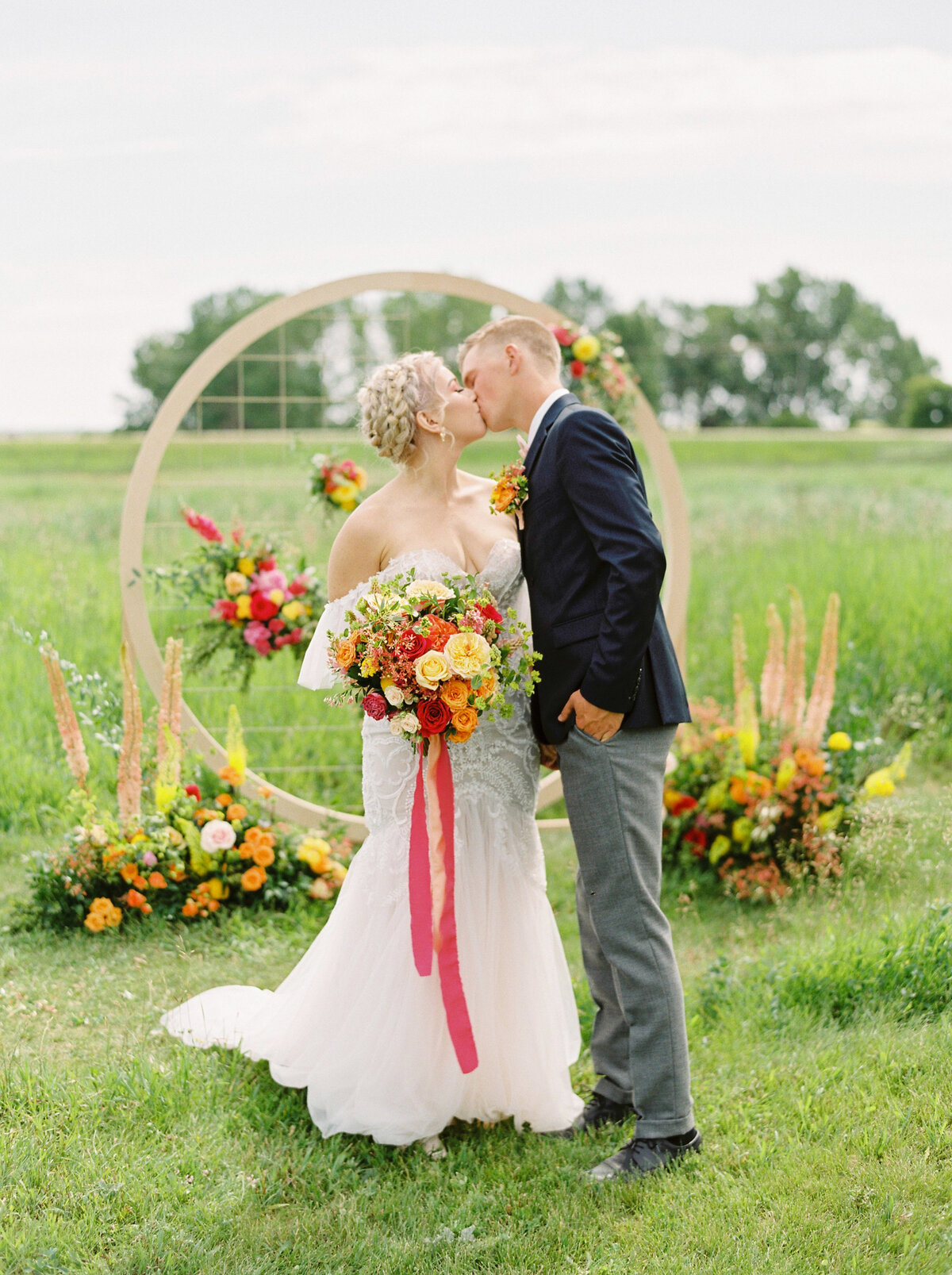 Couple kissing at their stunning and colourful red, orange and yellow outdoor wedding ceremony  at The Gathered, a nostalgic greenhouse based in Kathryn, Alberta wedding venue, featured on the Brontë Bride Vendor Guide.