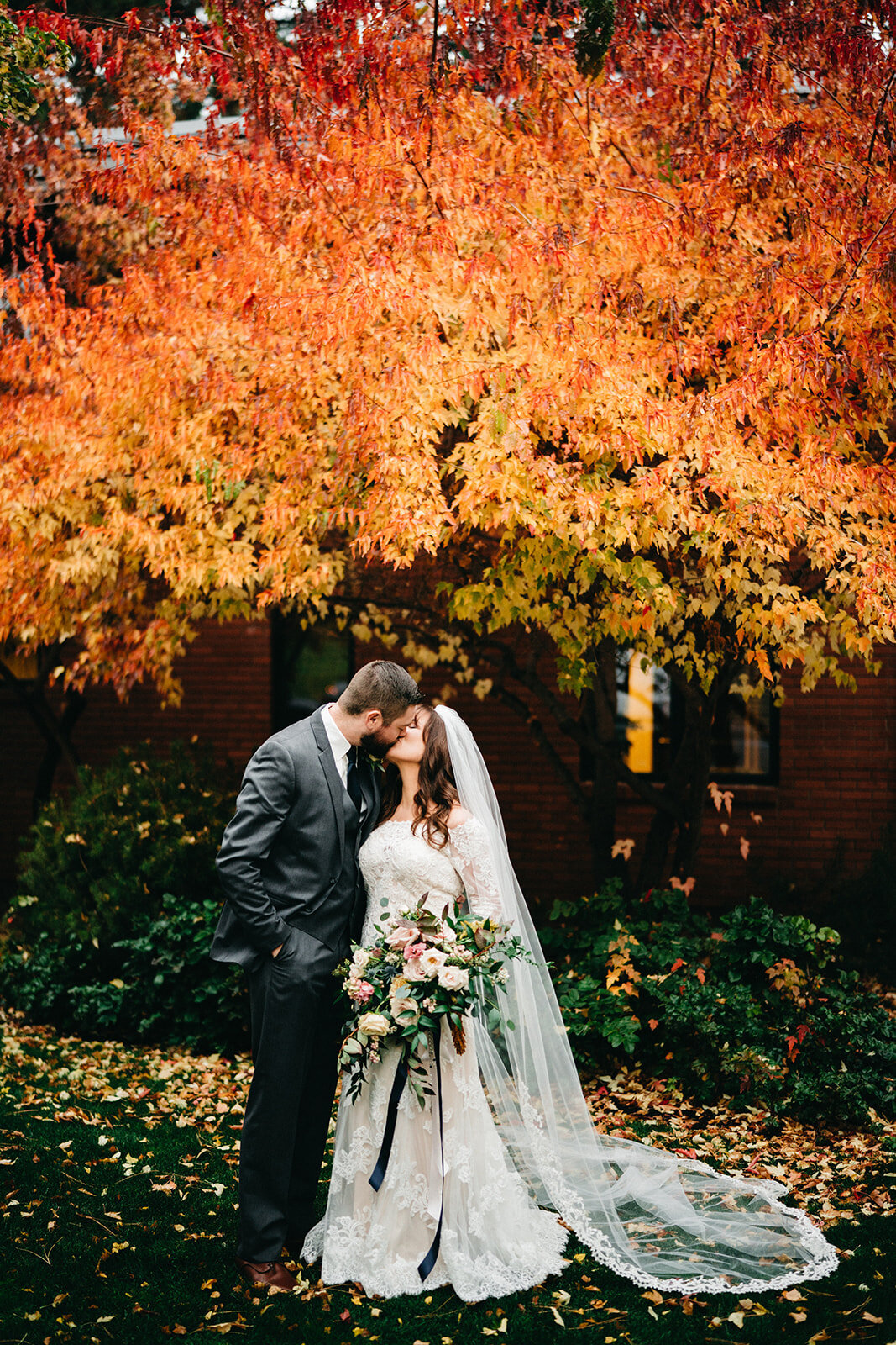 Bride and groom kissing in front of fall leaves at Old St Francis Church in Bend Oregon with bridal bouquet