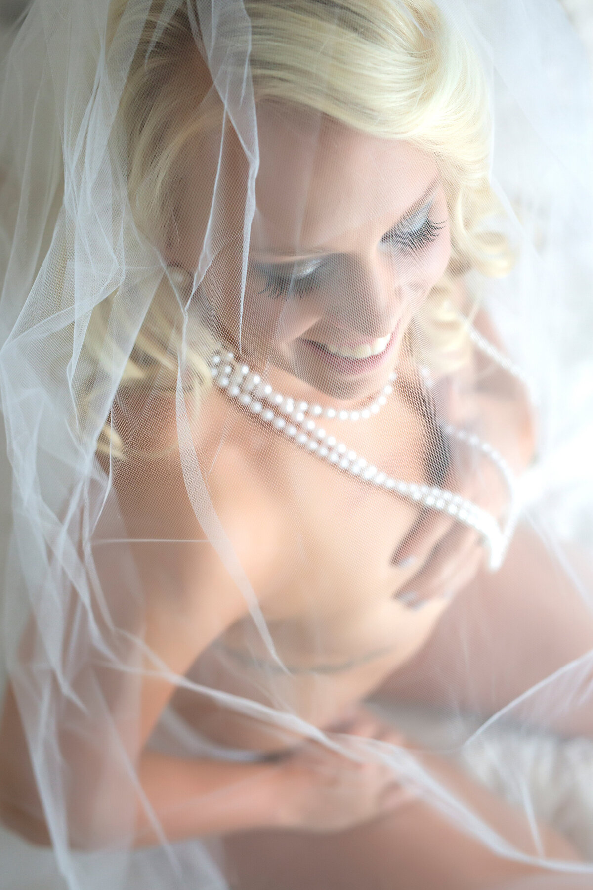 bride wearing a veil covering her and pearl necklace while smiling for her bridal boudoir session
