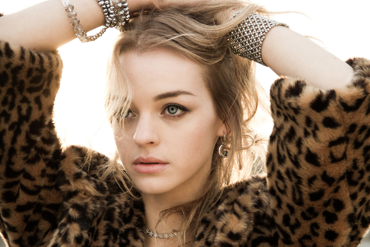 Olivia Rose Keegan musician portrait wearing leopard print faux fur jacket raised hands clasped against the back of her head