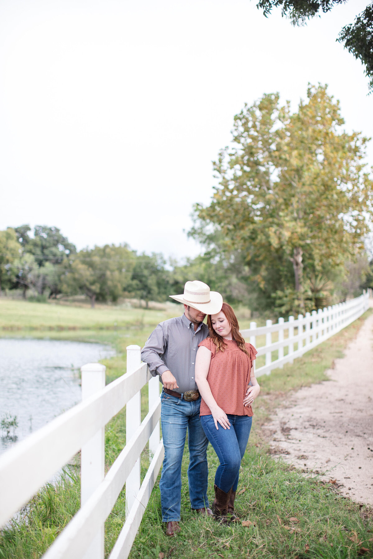 engagement session at Boerne wedding venue with white fence cowboy hat and boots by Firefly Photography