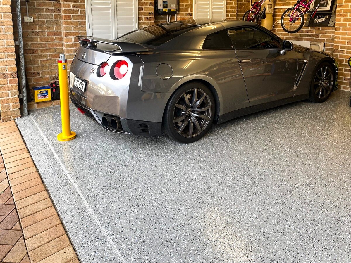 A high end vehicle parked in a garage with epoxy floors and a bollard behind it.