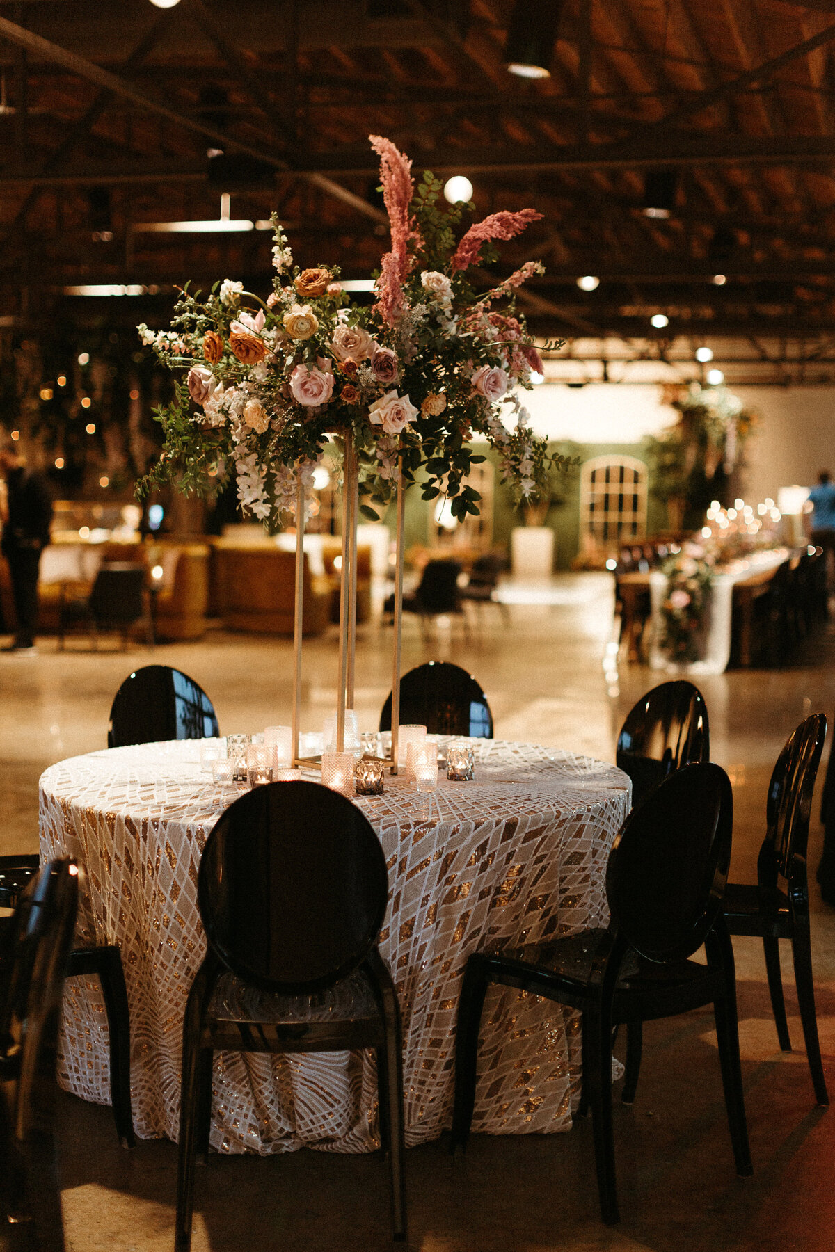 Stunning elevated centerpieces decorate this art deco wedding. Floral hues of terra cotta, mauve, burgundy, and dusty pink are brought to life with petal heavy roses, dried branches, and pink pampas grass. Designed by Rosemary and Finch in Nashville.