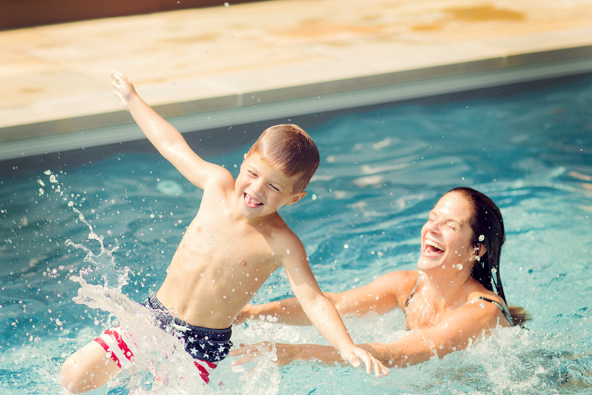 Mom is throwing her son in the air in their pool, both laughing!