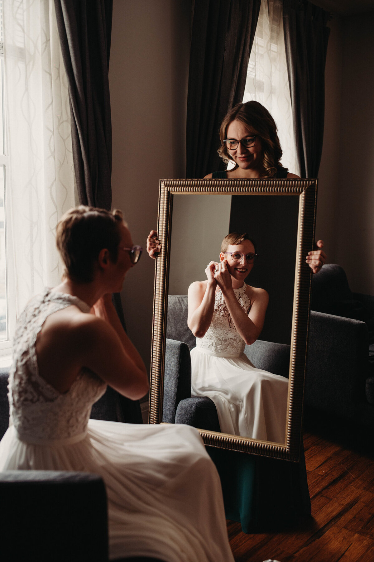 Bride puts on earrings with help from friend in air bnb in tremont for wedding