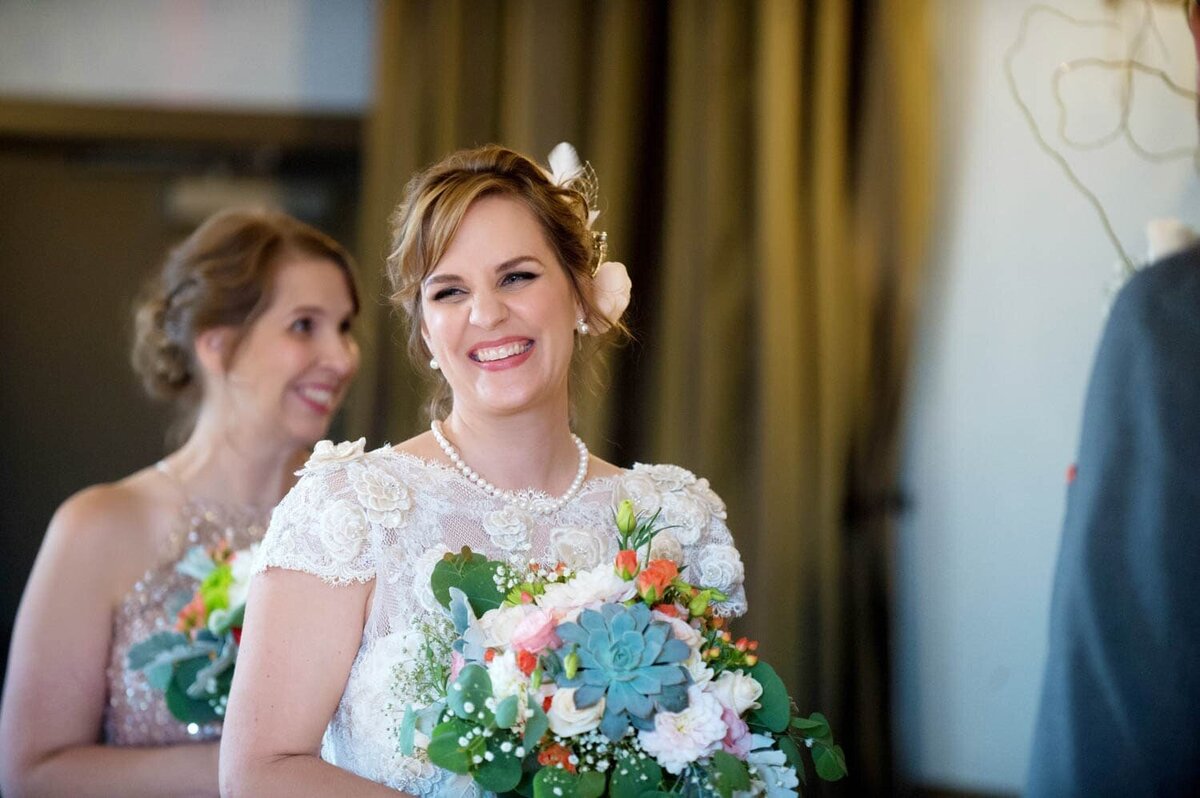 a bride holding a pretty succulent bouquet wearing a vintage dress laughs during the ceremony