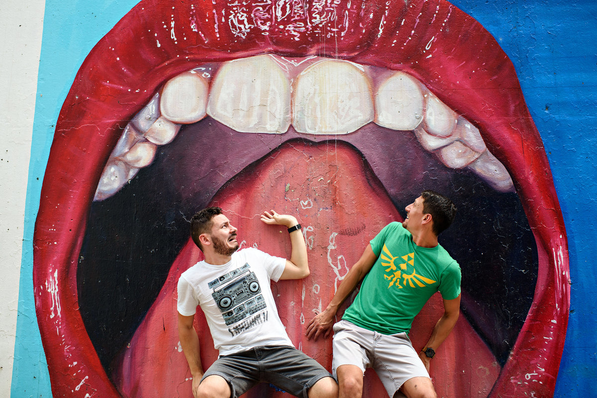 A fun same sex couple act silly in front of a large graffiti mouth in Chicago.