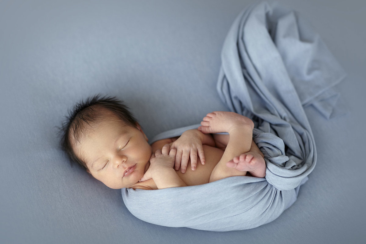 Newborn baby boy wrapped in a blue blanket sleeping