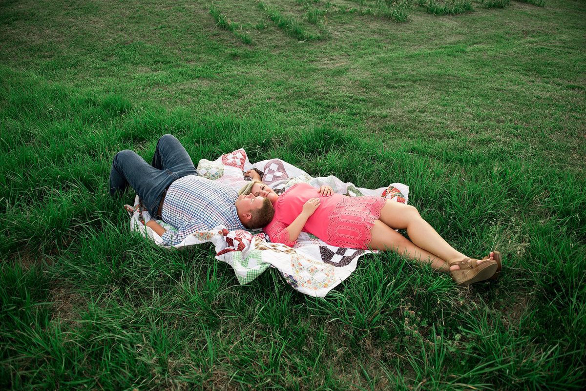 Couple lying together on a vintage quilt in the middle of a grassy field
