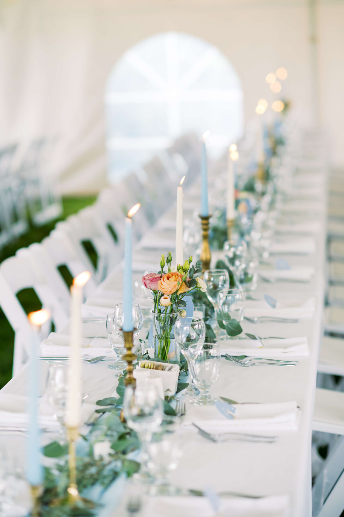 Wedding reception table with blue runner, greenery, candles and glasses