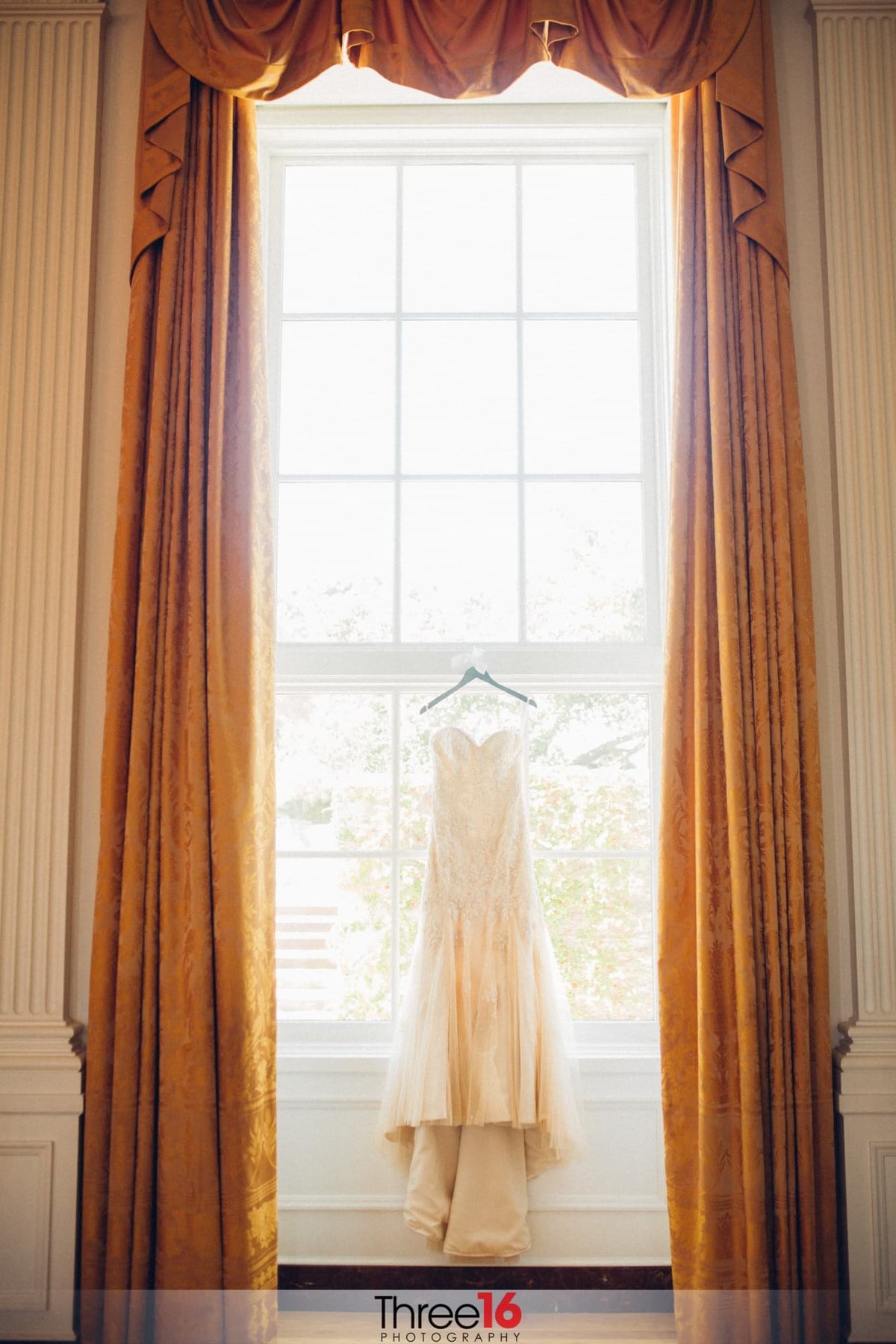 Bride's dress hangs on display in front of a large window