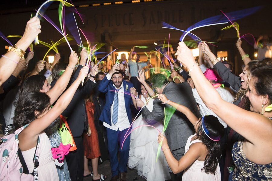 A bride and groom exit their wedding reception through a tunnel of guests holding glow sticks.