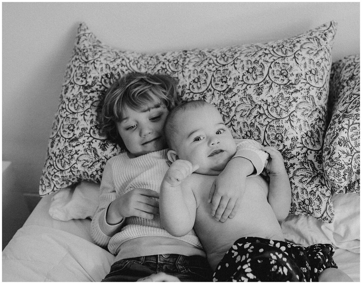 Toddler with arm around baby lying on bed at sweet home family session in Austin by Amber Vickey Photography